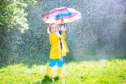 Fotolia Funny cute curly toddler girl wearing yellow waterproof coat and boots holding colorful umbrella playing in the garden by rain and sun weather on a warm autumn or sumemr day